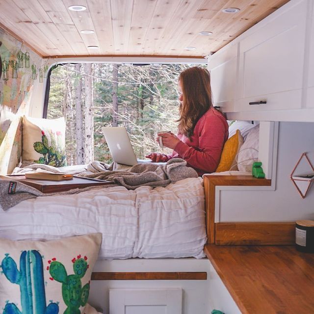 a woman sitting on top of a bed next to a window with a laptop computer