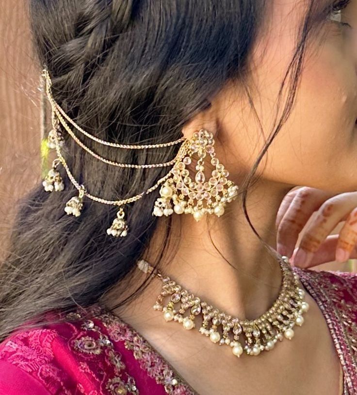 a woman in a pink sari with gold jewelry on her neck and hands to her ear