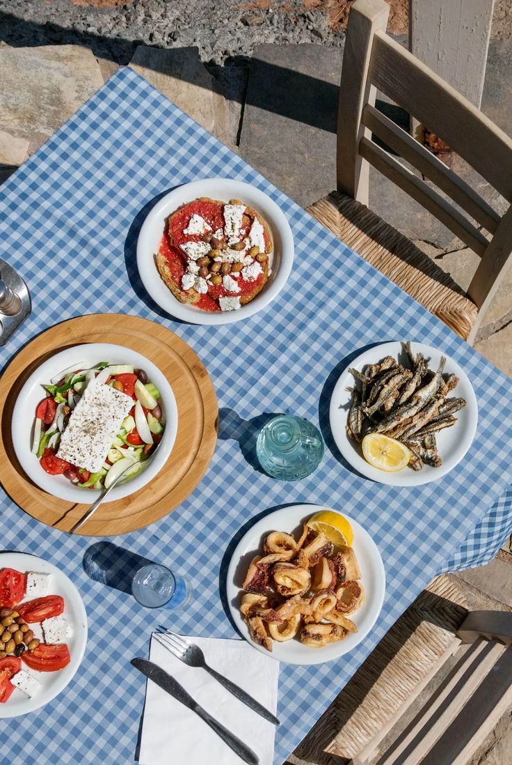 an outdoor table with plates of food on it and utensils next to them