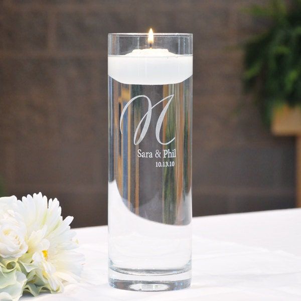 a candle is sitting on a table next to a vase with white flowers and greenery