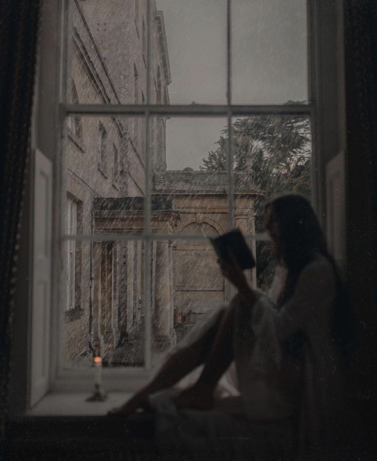 a woman sitting on a window sill reading a book in front of an open window