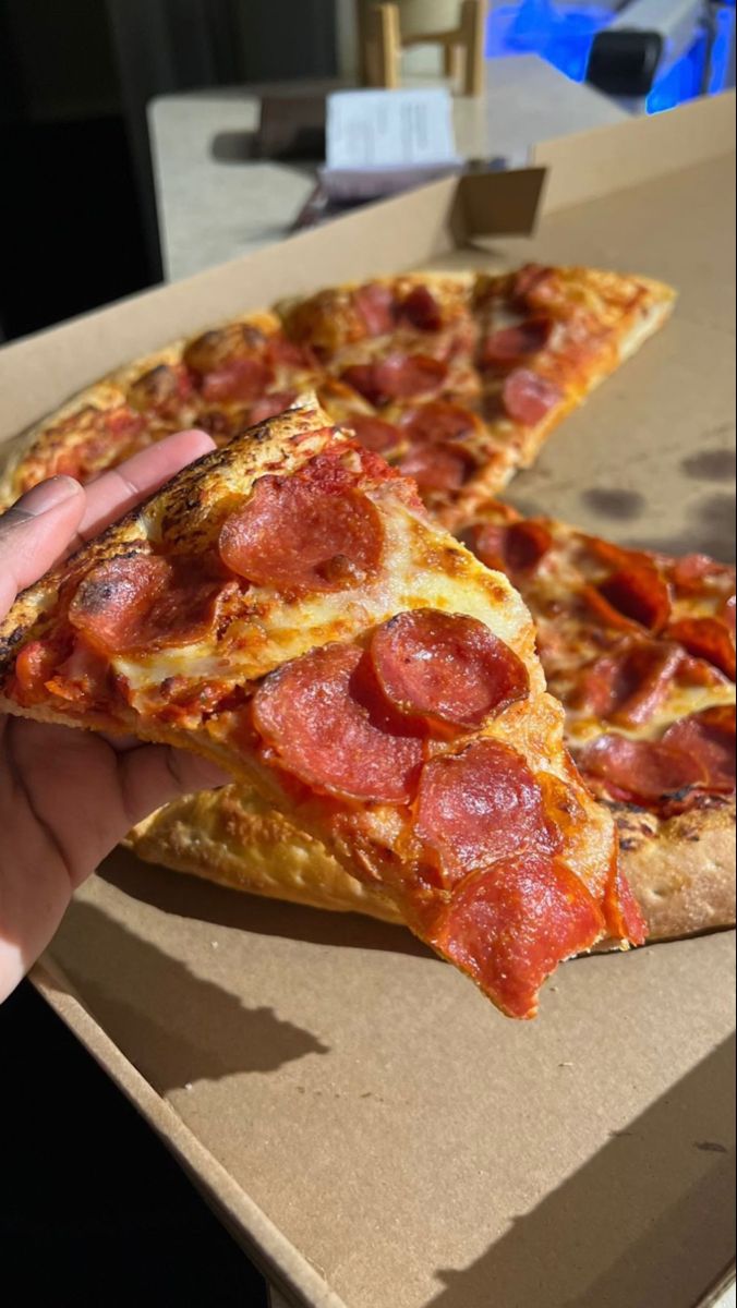 a slice of pepperoni pizza being held up by someone's hand in a box