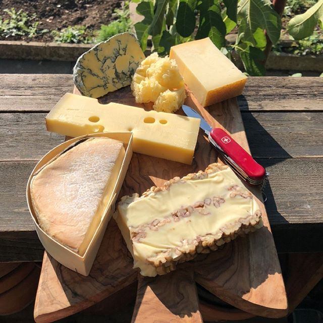 several different types of cheese are on a wooden platter with a knife and fork