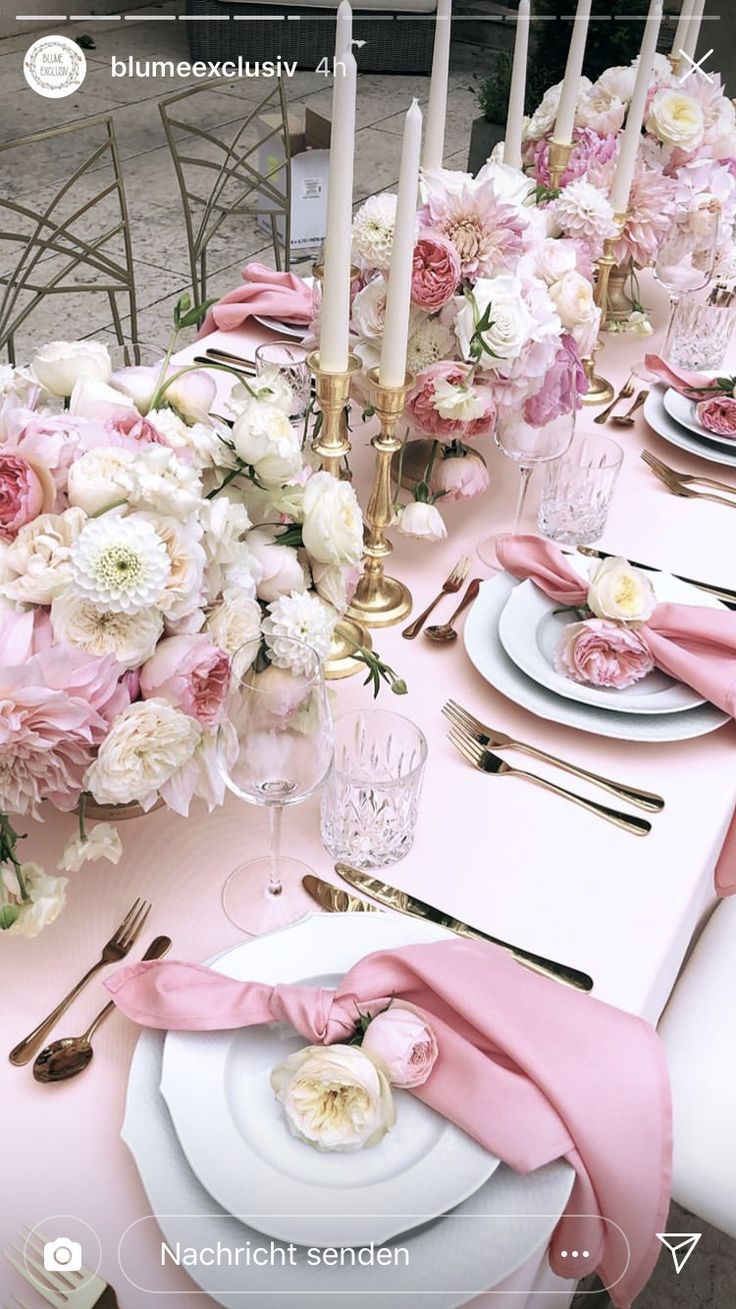 the table is set with pink napkins and white plates, silverware, and flowers