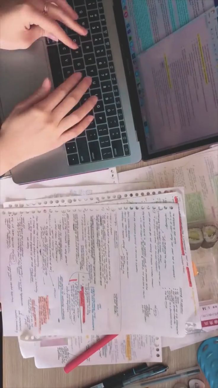 a person typing on a laptop computer next to papers