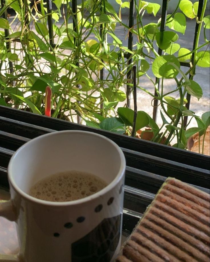 a cup of coffee sitting on top of a window sill next to a cracker