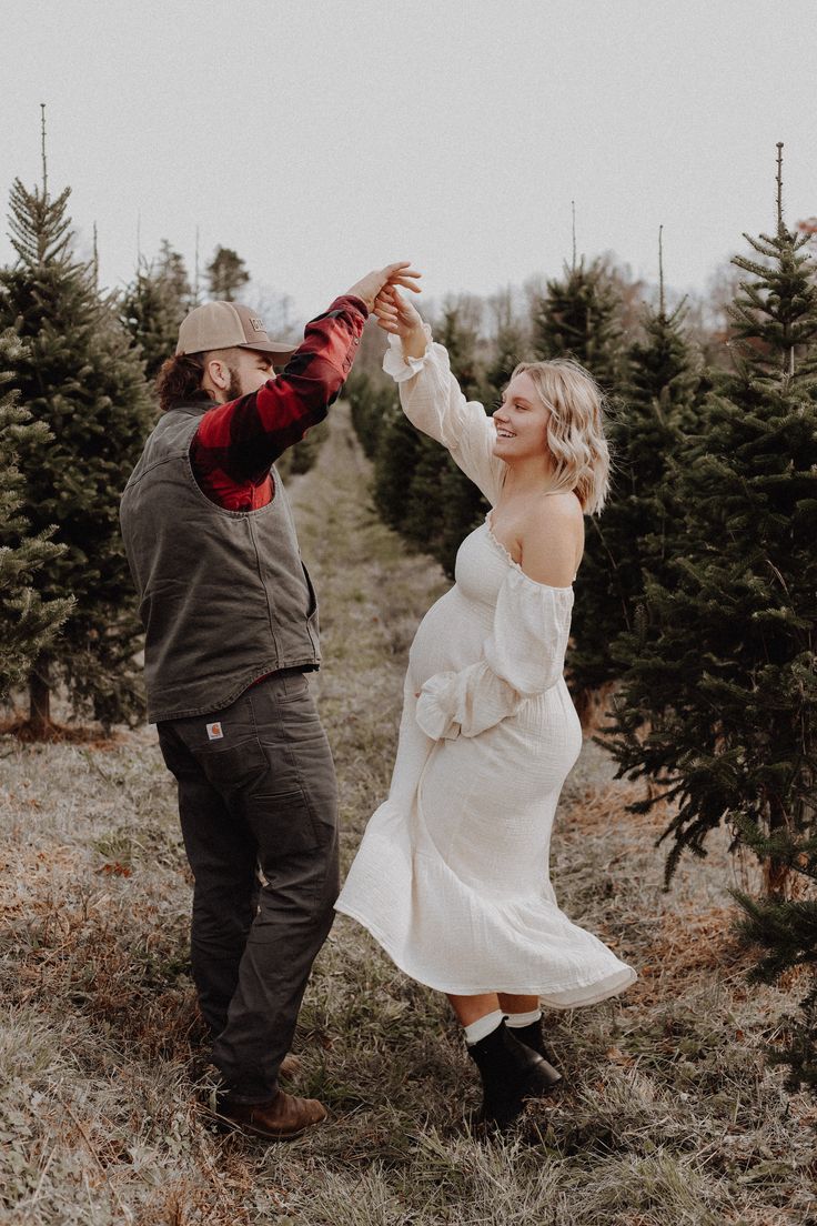 a man and woman are holding hands in the middle of a field surrounded by trees