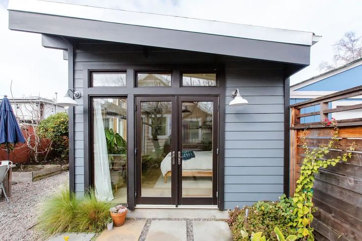 a small gray house with sliding glass doors and an outdoor living area in the back