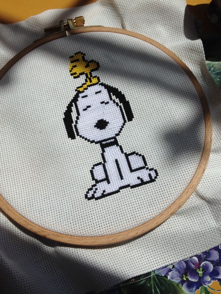 a cross stitch dog with a crown on it's head sitting in front of a white cloth