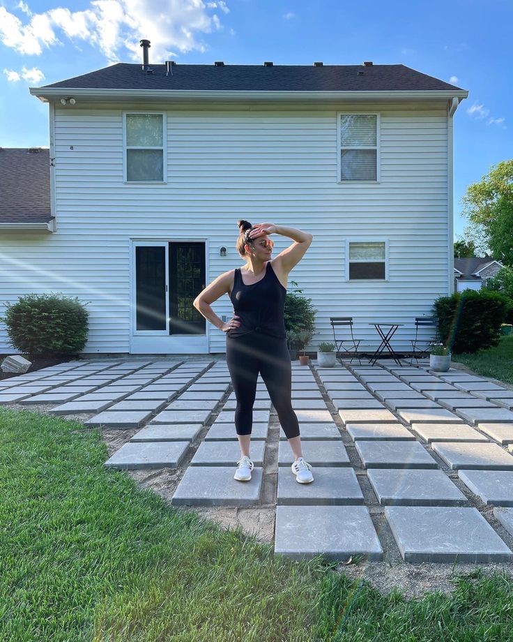 a woman standing in front of a house with her hands on her head and looking off into the distance