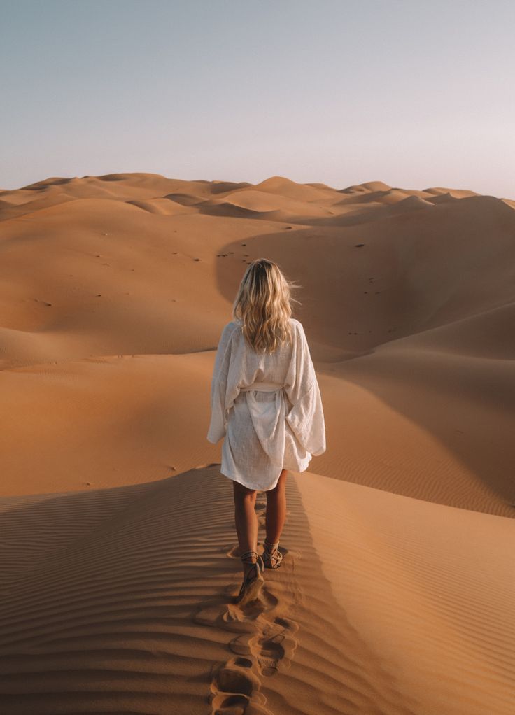 a woman walking in the desert with sand dunes