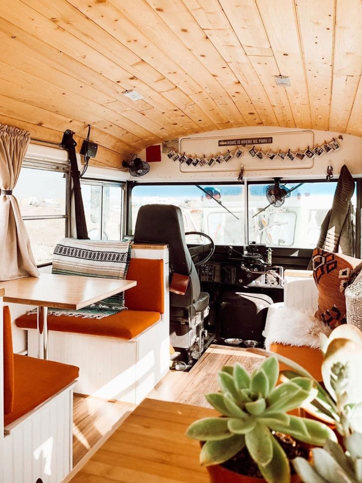 an interior view of a recreational vehicle with wood paneling and white walls, windows, and wooden flooring