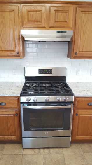 a stove top oven sitting inside of a kitchen next to wooden cupboards and counter tops