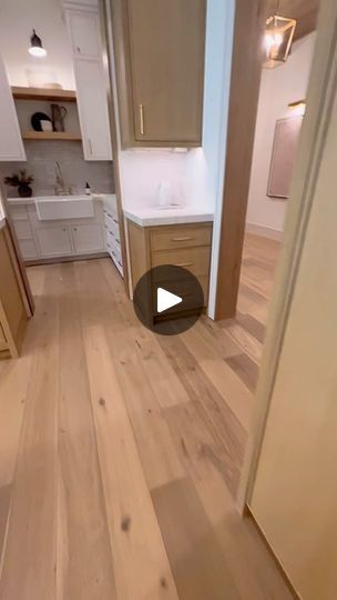 an empty kitchen and living room with wood flooring in the foreground, white cabinets on the far wall