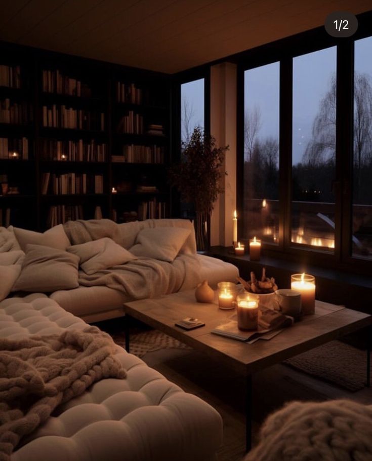 a living room filled with lots of furniture and lit candles in front of large windows