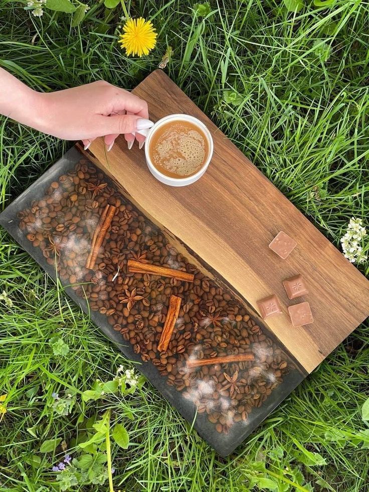 a cup of coffee and some cinnamon sticks on a tray in the grass with flowers