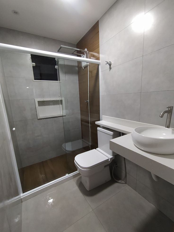 a white toilet sitting next to a sink in a bathroom near a shower stall with a glass door