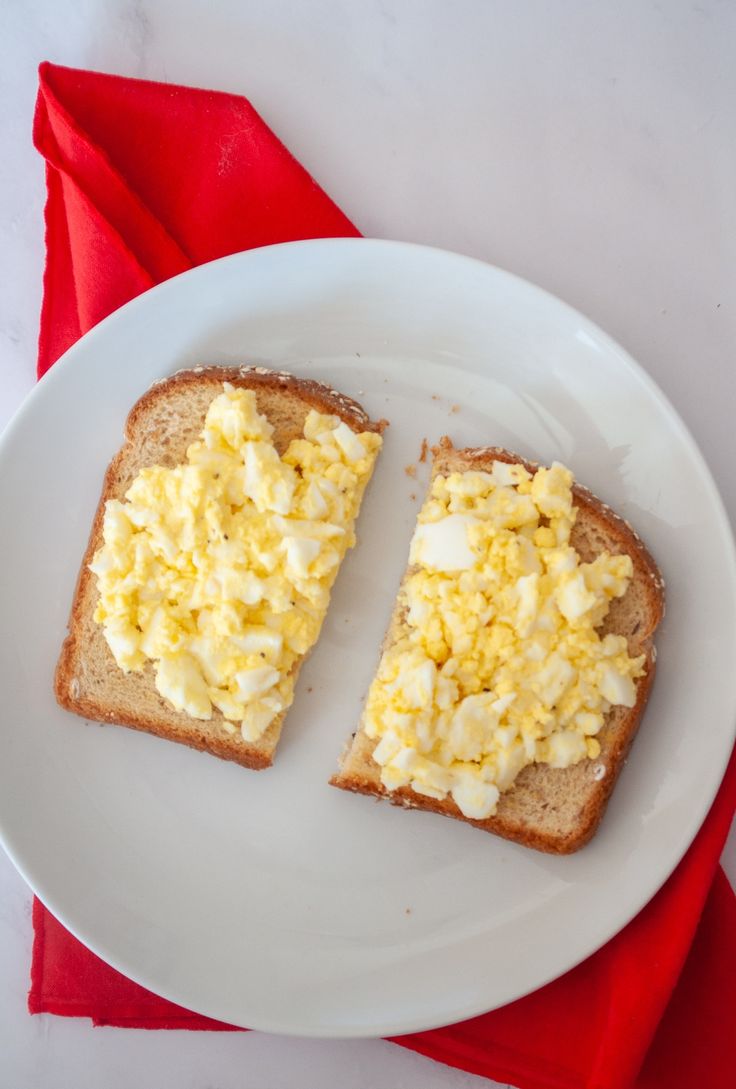 two slices of toast with scrambled eggs on them sitting on a white plate next to a red napkin