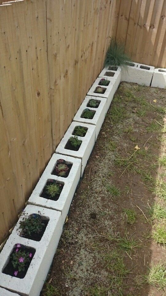 several planters are placed in the corner of a fenced area, with grass growing between them