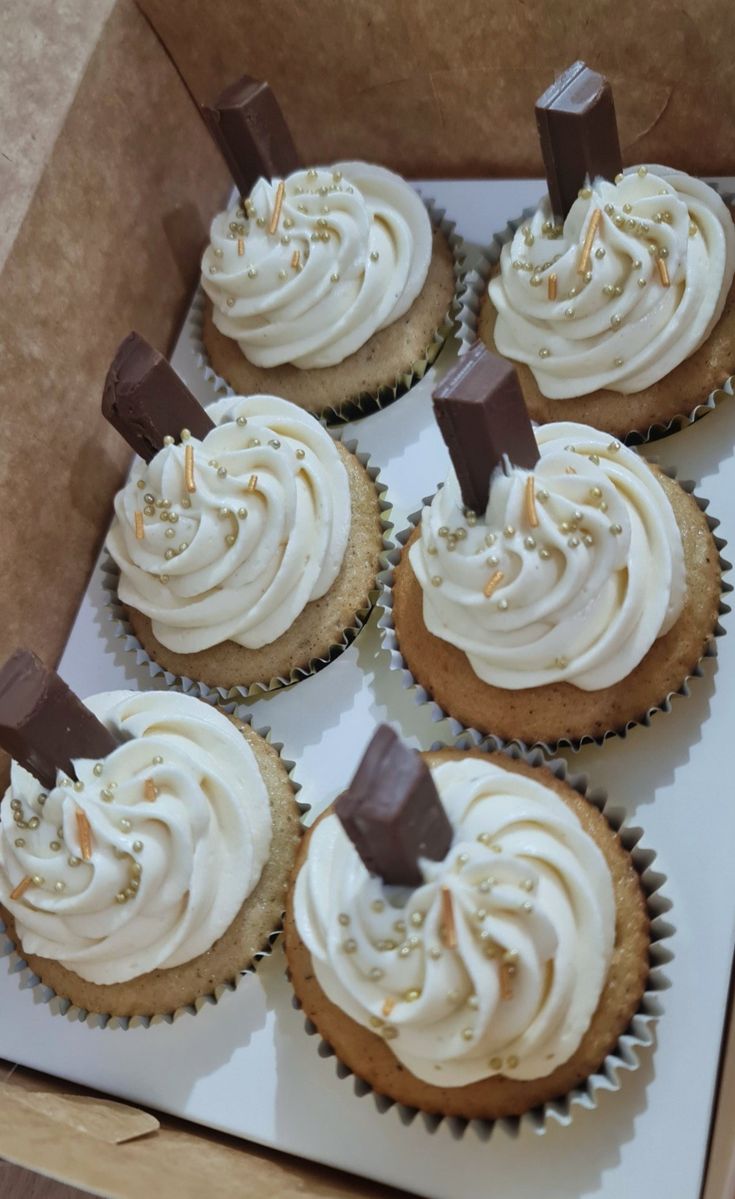 six cupcakes with white frosting and chocolate on top in a cardboard box