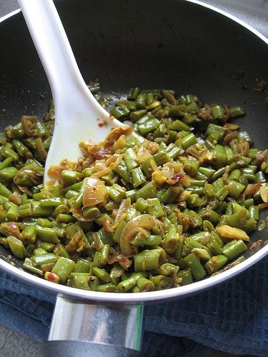 green beans are being cooked in a skillet with a white spoon on the side