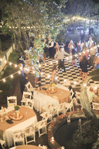 an outdoor party with tables and chairs, lit up by fairy lights at night time