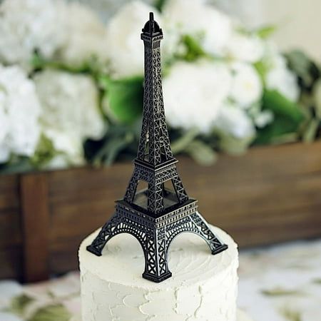 a white cake with a black eiffel tower on top and flowers in the background