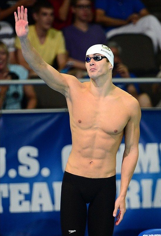 a shirtless male swimmer waves to the crowd