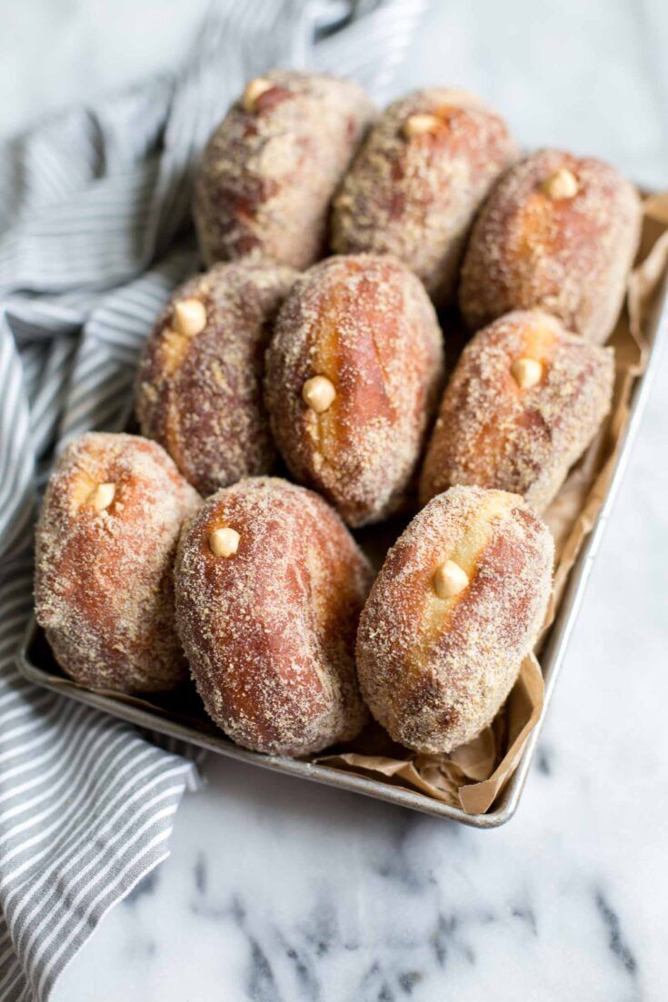 powdered sugar covered doughnuts in a tray on a marble counter top with a striped napkin