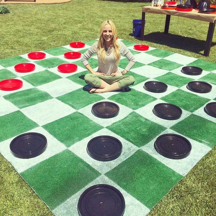 a woman sitting on top of a giant checkered board game in the grass with red and black circles