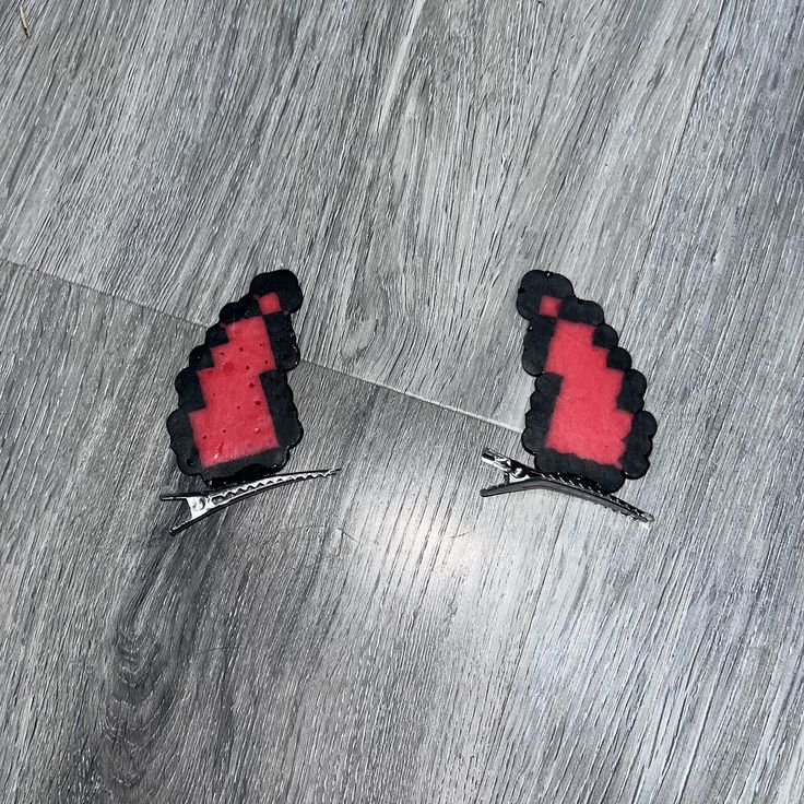 two pairs of red and black earrings sitting on top of a wooden floor next to each other