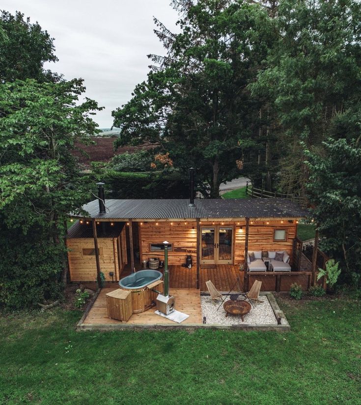 a small wooden cabin in the middle of some trees, with a hot tub and seating area