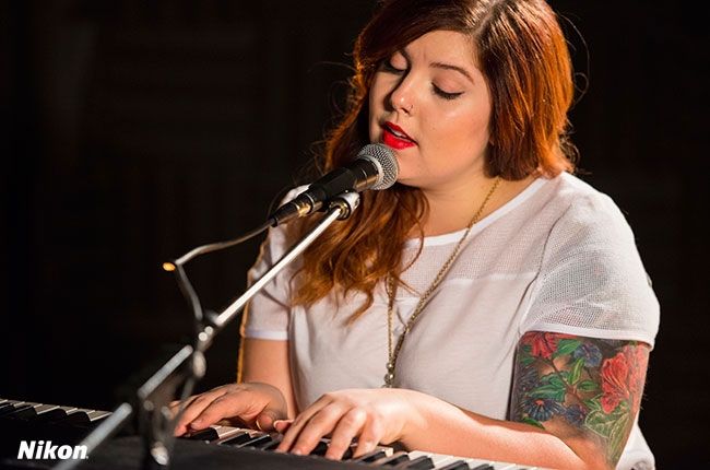 a woman sitting at a keyboard with a microphone in front of her and singing into a mic