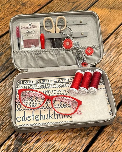 an open suitcase with red thread, scissors and eyeglasses in it on a wooden table