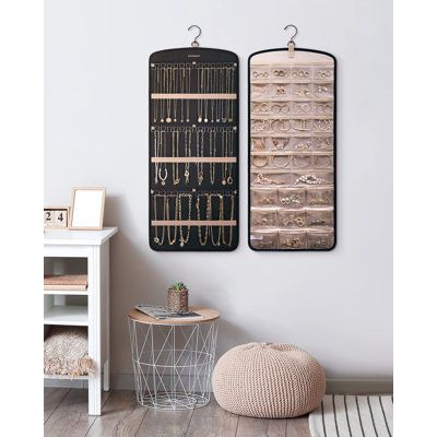 two wooden wall hangings with earrings on them and a round ottoman in the foreground