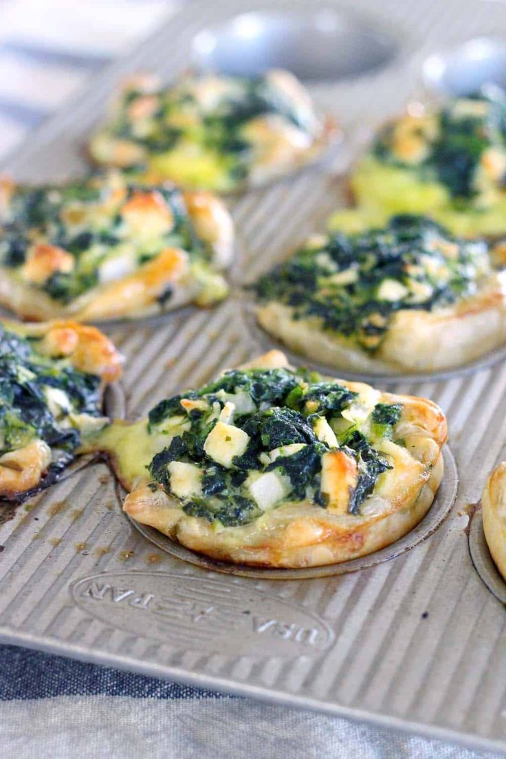 several mini pizzas with spinach and cheese on them sitting on a baking sheet