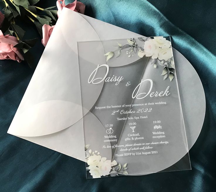 a wedding card with flowers on it sitting next to a bouquet of pink and white roses