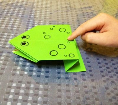 a hand is pointing at an origami frog on a table with polka dots