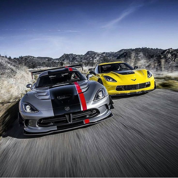 two sports cars driving down the road with mountains in the background