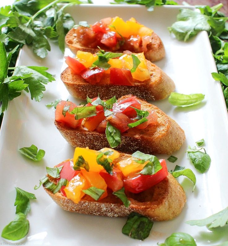 three pieces of bread with tomatoes and basil on them sitting on a white platter