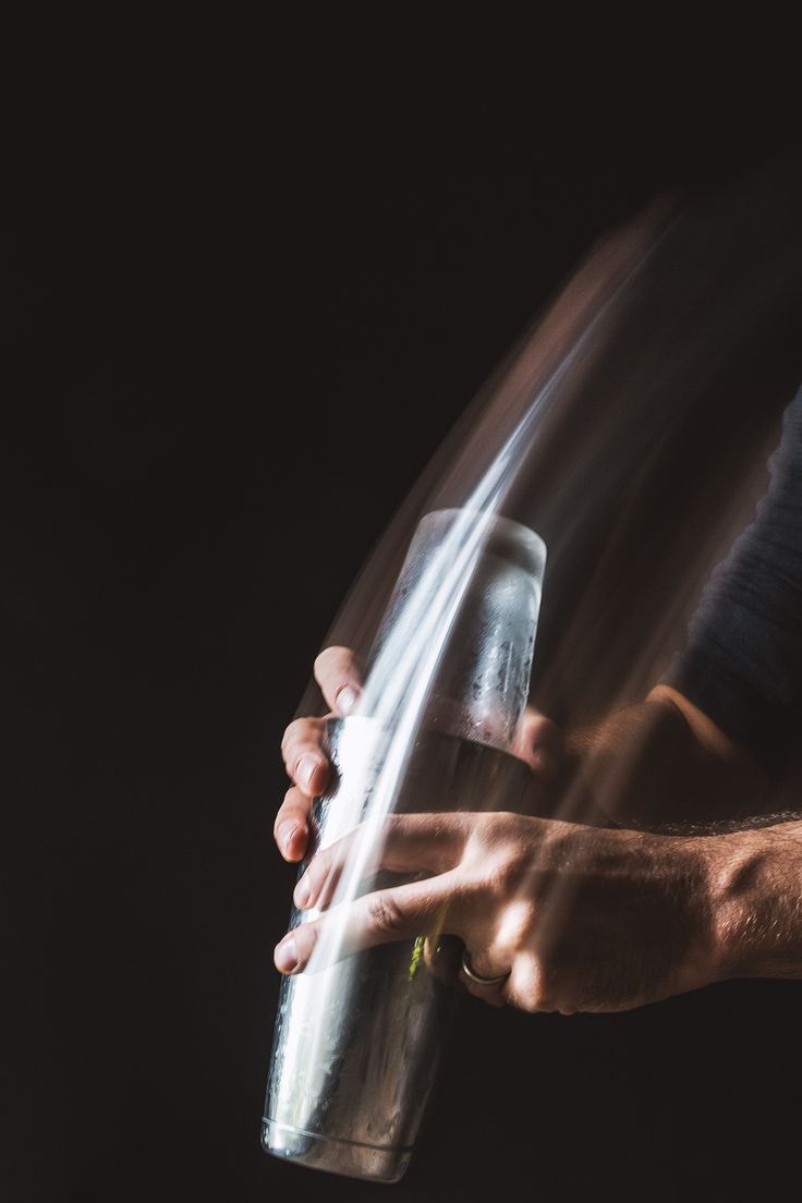 a person holding a glass in their hand with the light coming from behind it on a black background