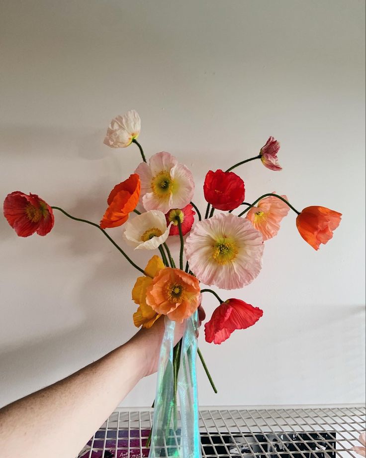 a person holding a vase with flowers in it on a table next to a wire rack