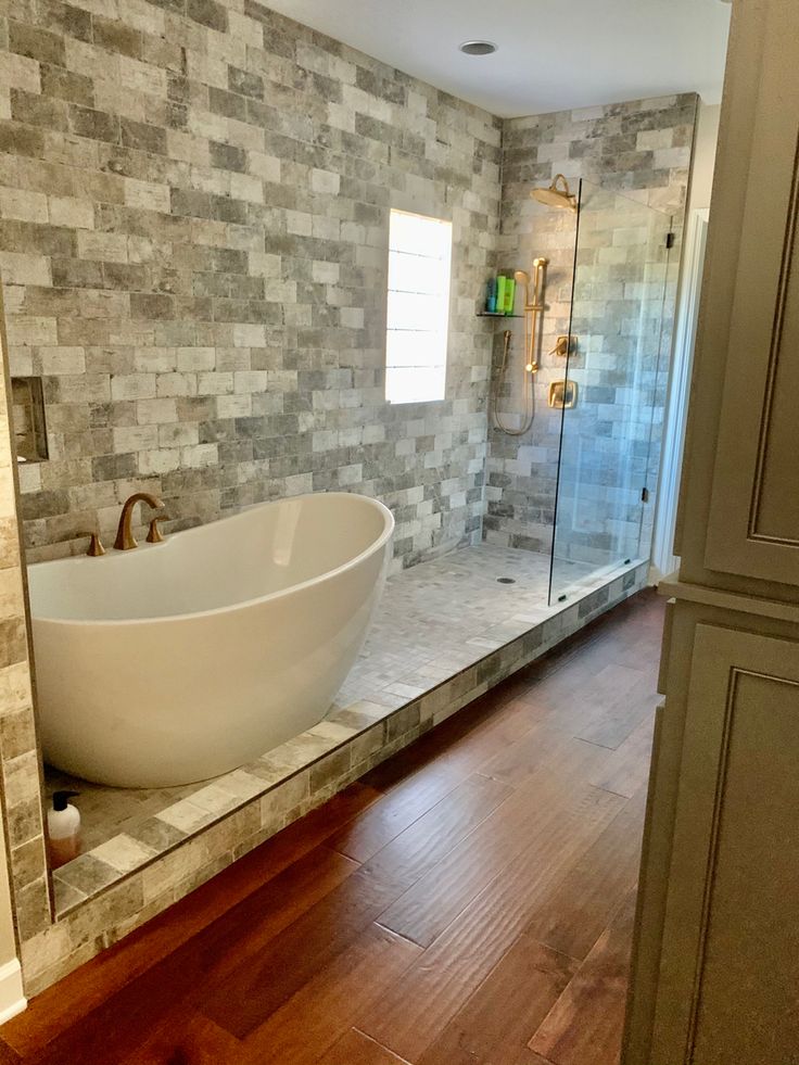 a large bath tub sitting on top of a wooden floor next to a walk in shower