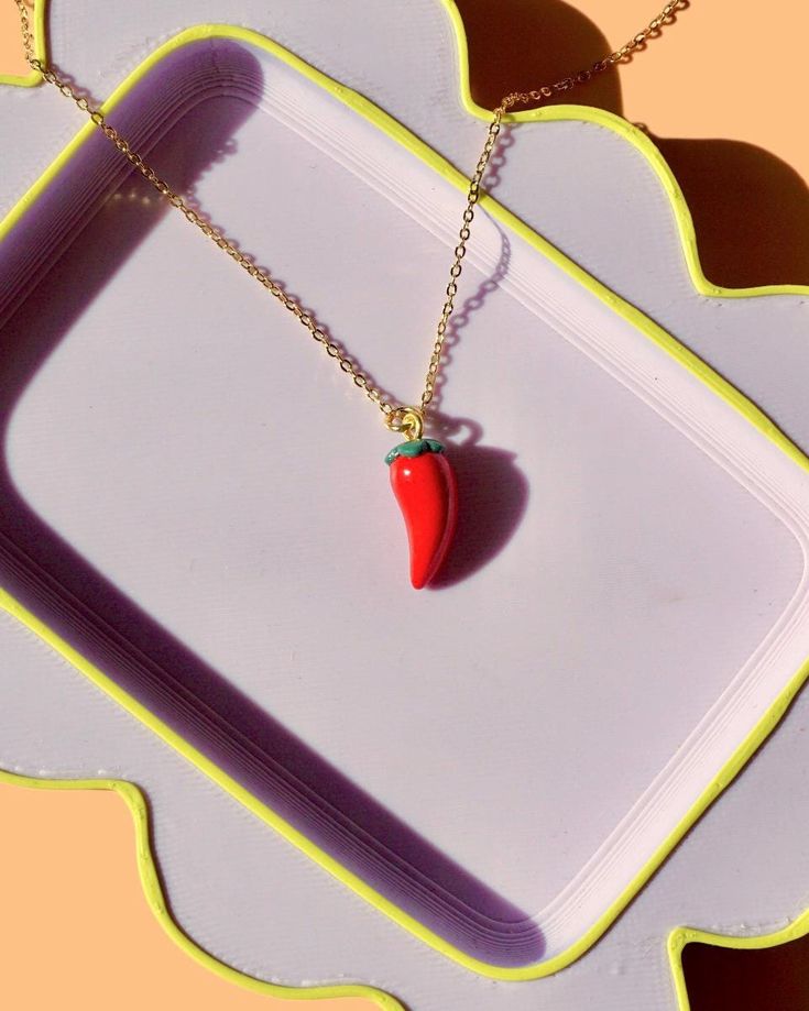 a necklace with a red pepper hanging from it's side on a white tray