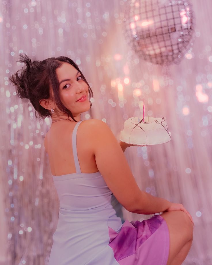 a woman sitting on the floor with a cake in her hand and disco balls behind her