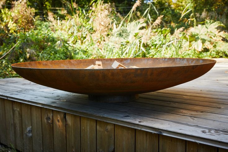 a large metal bowl sitting on top of a wooden table in front of some plants