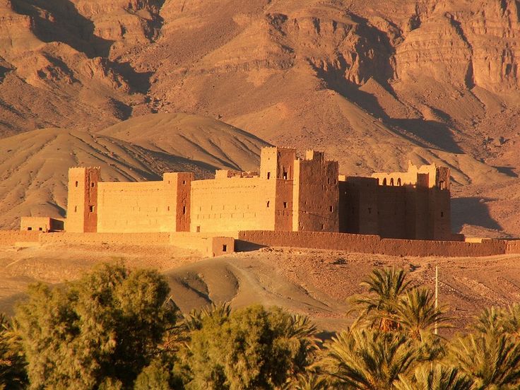 an adobe style building in the desert with mountains in the backgrouds and palm trees