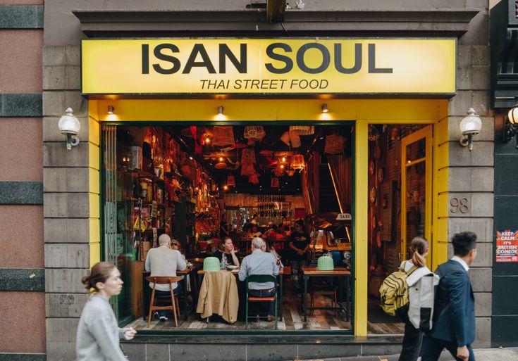 people are walking past a store front with yellow and green doors that says isan soul