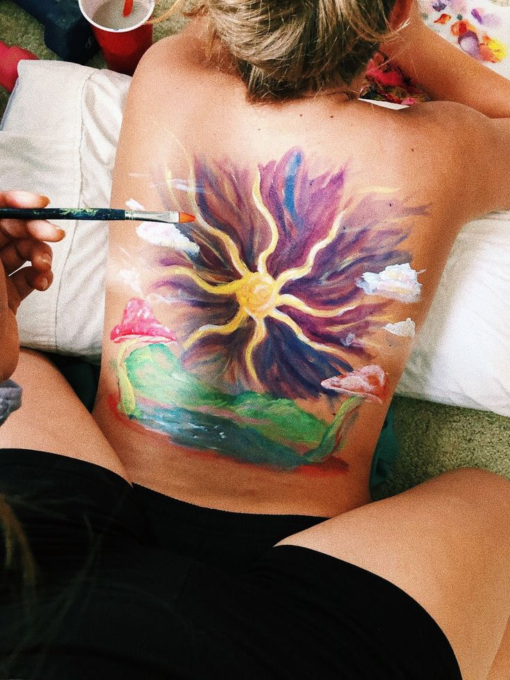 a woman sitting on the floor with her back painted like a flower and holding a paintbrush