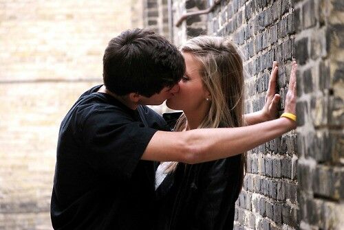 a man and woman kissing against a brick wall